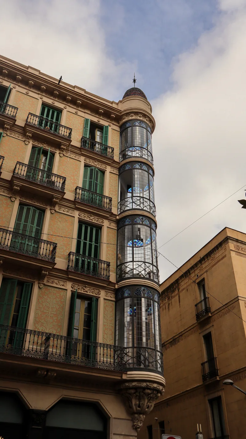 Ornate apartment building with balconies and a glazed corner turret, looking up against the sky