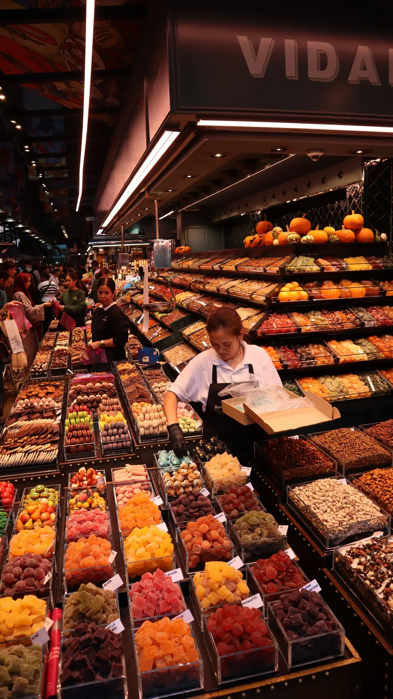 A vendor arranging dried fruit and sweets at a brightly lit market stall
