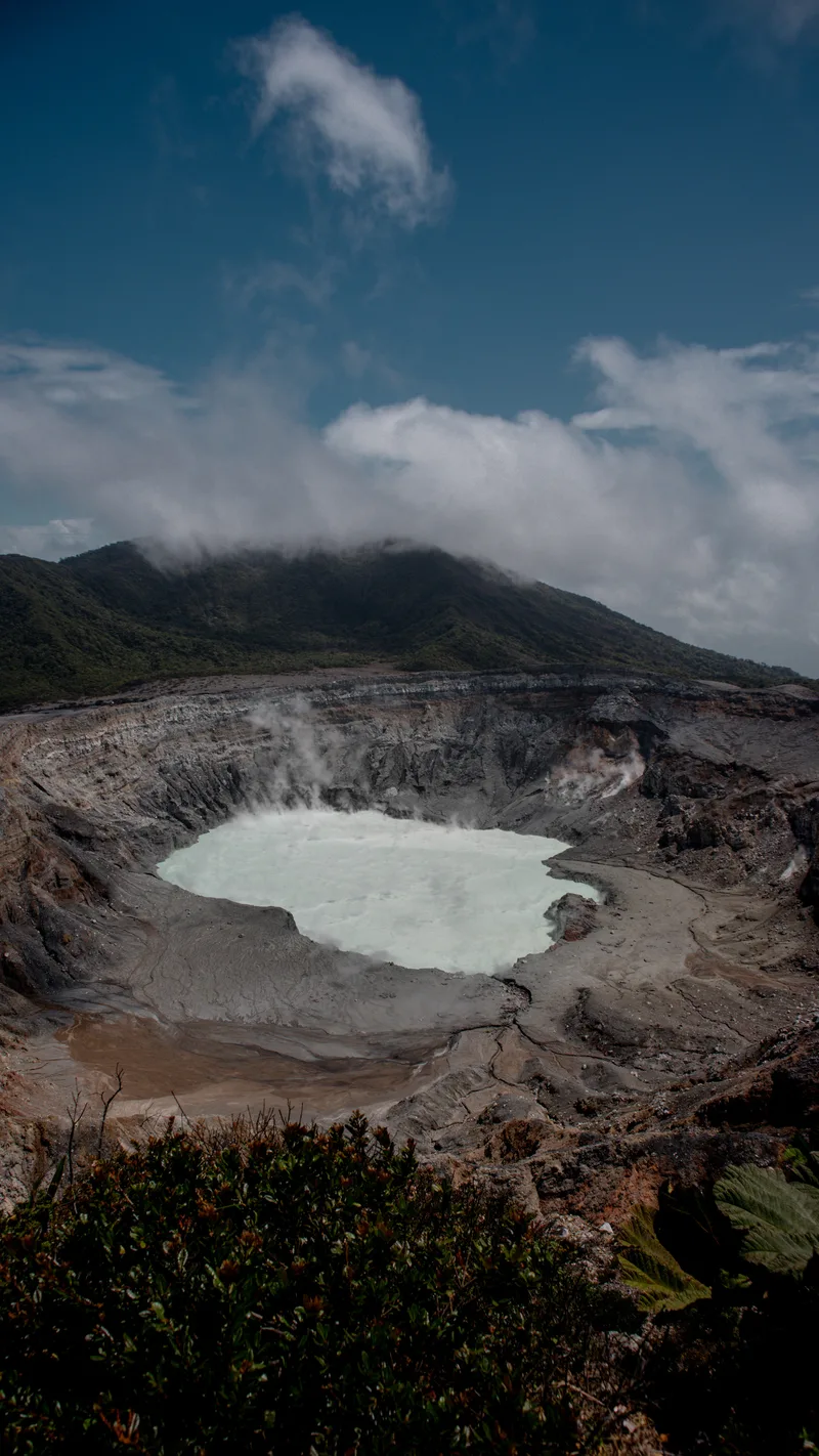 The pale crater lake of Poás Volcano under drifting cloud