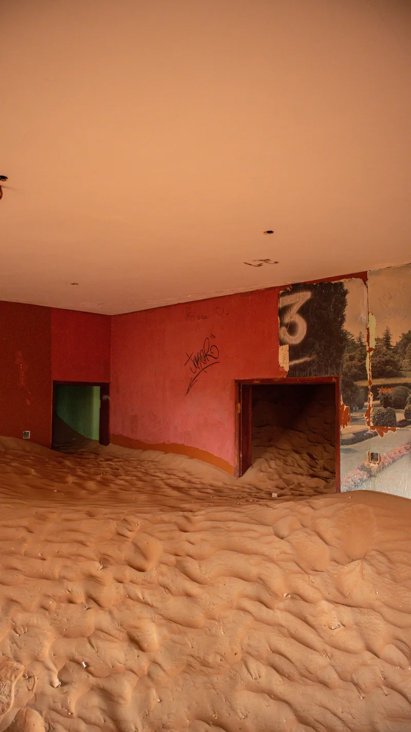 Sand drifted into the rooms of an abandoned house with red walls