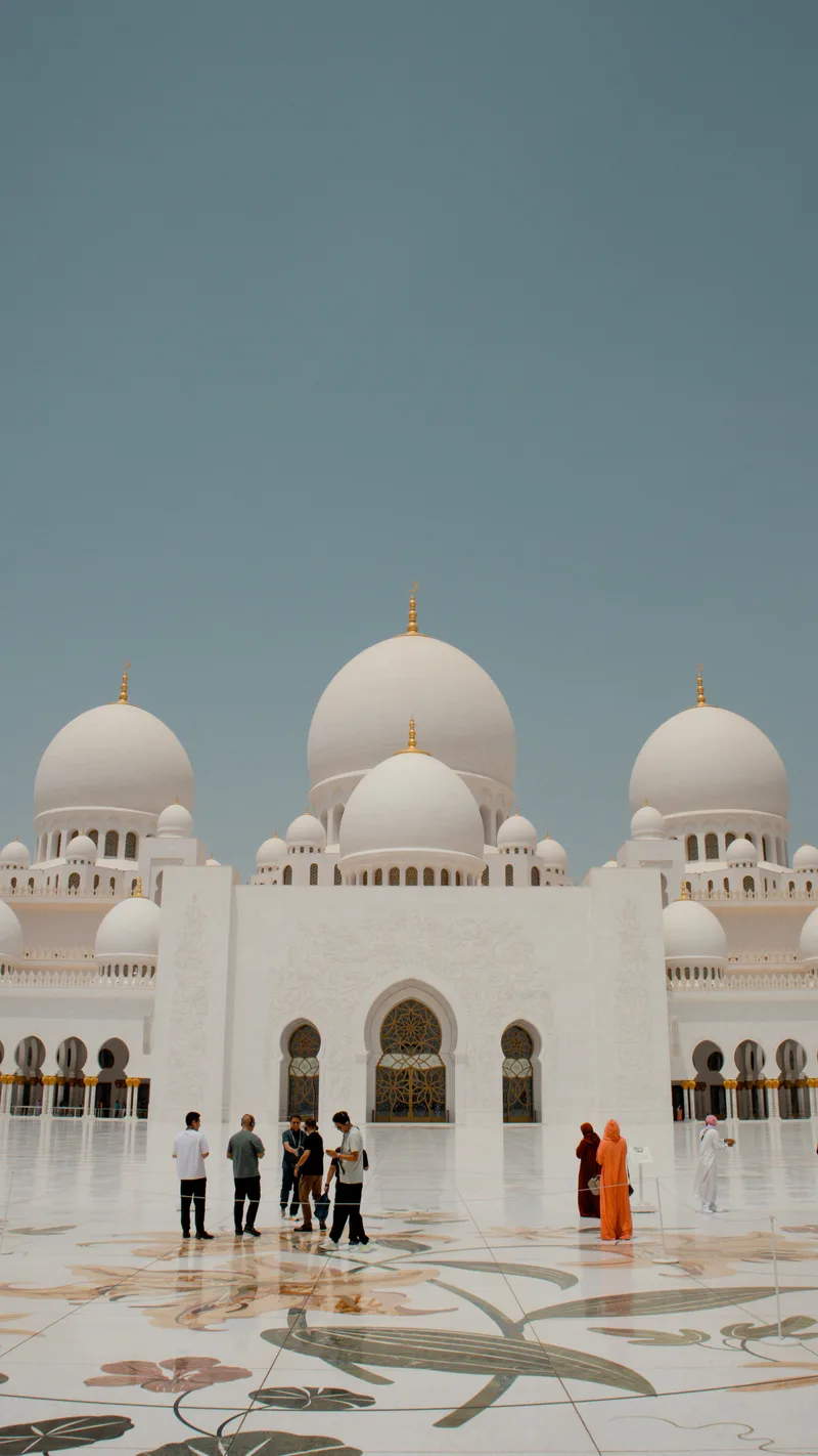 White marble domes and courtyard of the Sheikh Zayed Grand Mosque with visitors