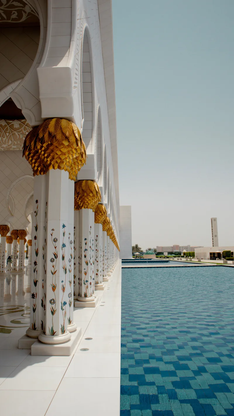 Marble columns with gold palm-shaped capitals beside a blue reflecting pool