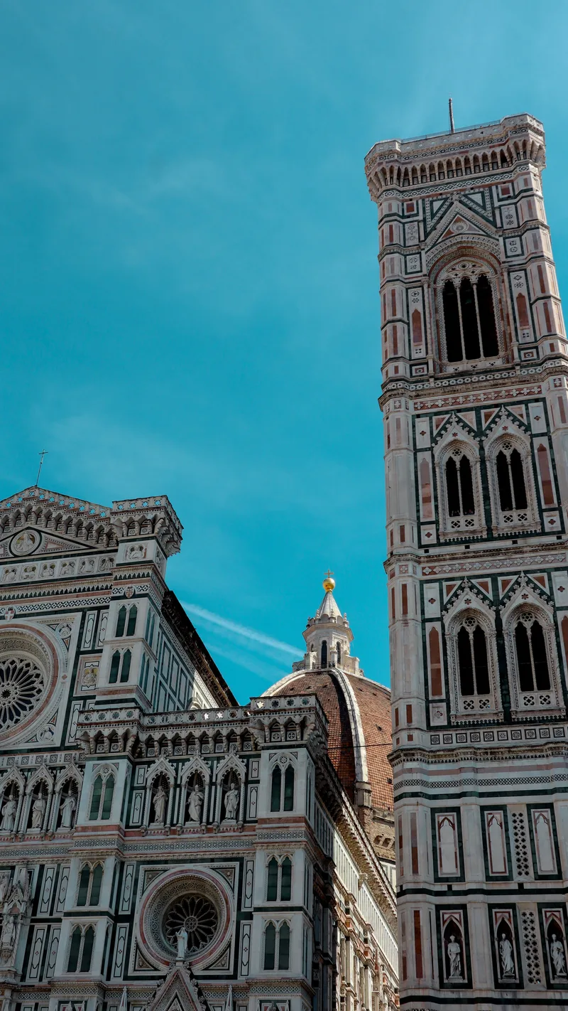 The marble facade of Florence Cathedral beside the bell tower, against a deep blue sky