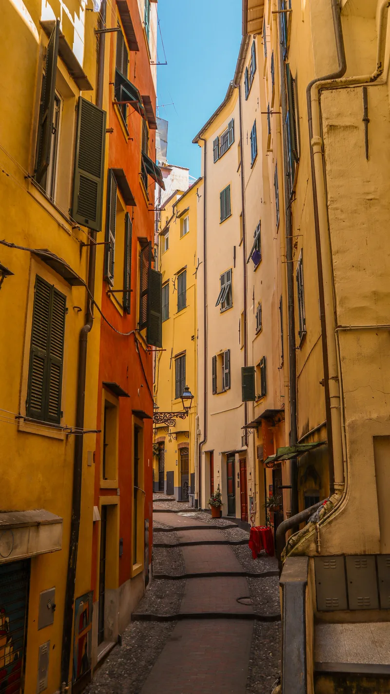 A narrow lane between tall yellow and orange buildings with green shutters