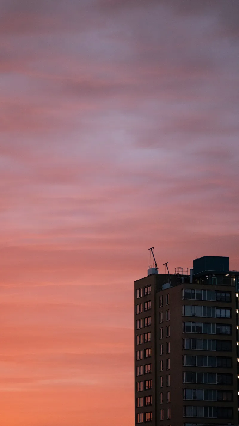 A tower block against a pink and orange sunset sky