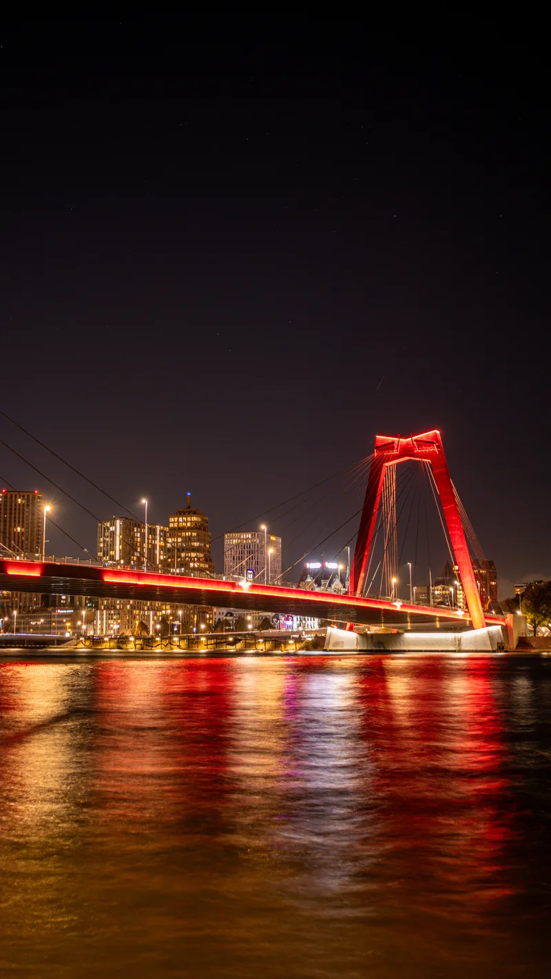 The red Willemsbrug lit up at night and reflected in the river