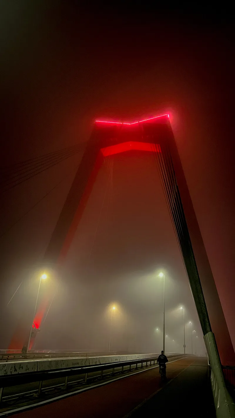 The red-lit pylon of the Willemsbrug in thick fog