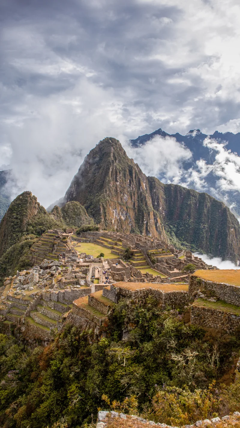 The ruins of Machu Picchu beneath Huayna Picchu, with clouds over the mountains