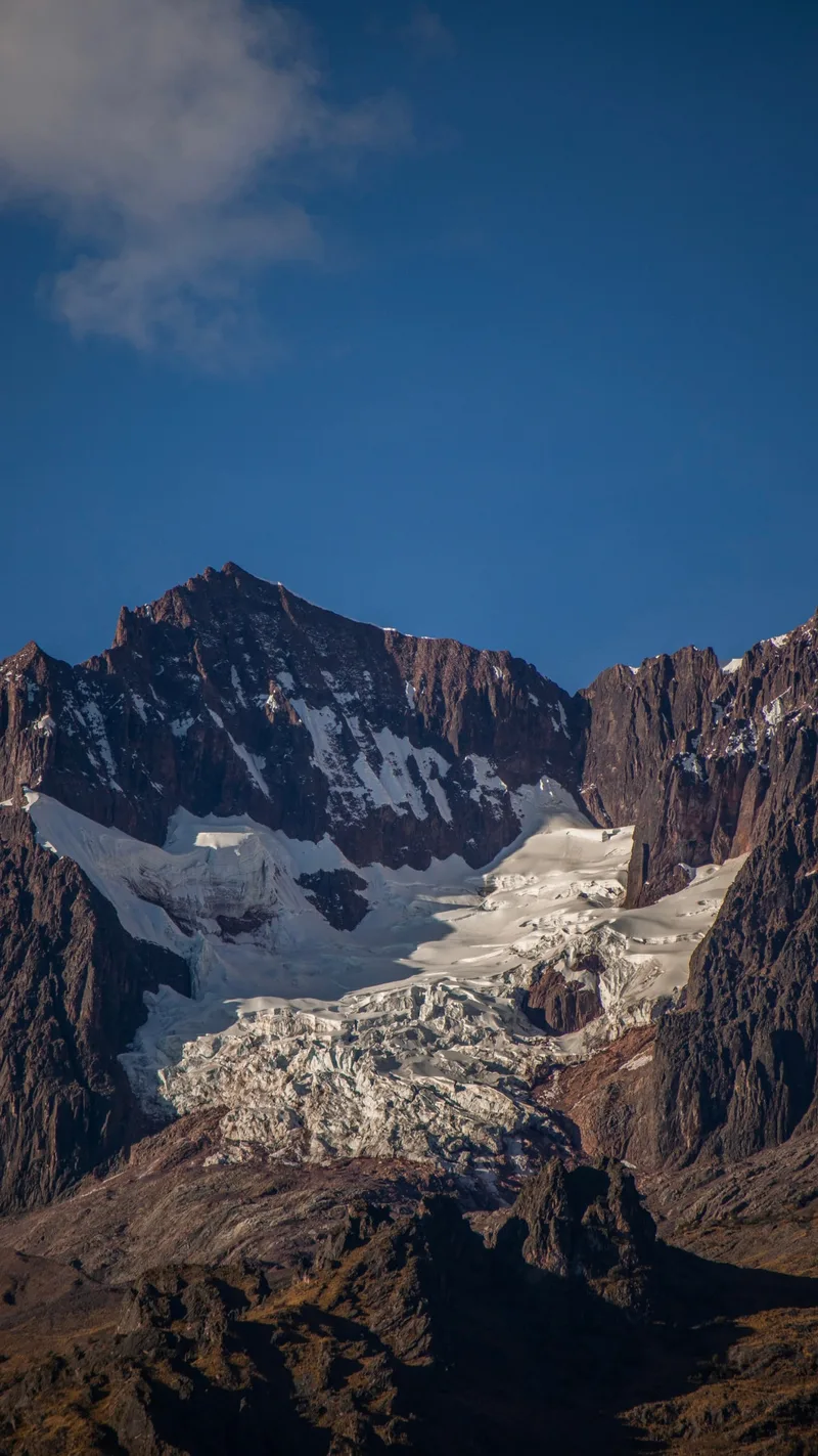 A glacier between dark rocky peaks under a blue sky