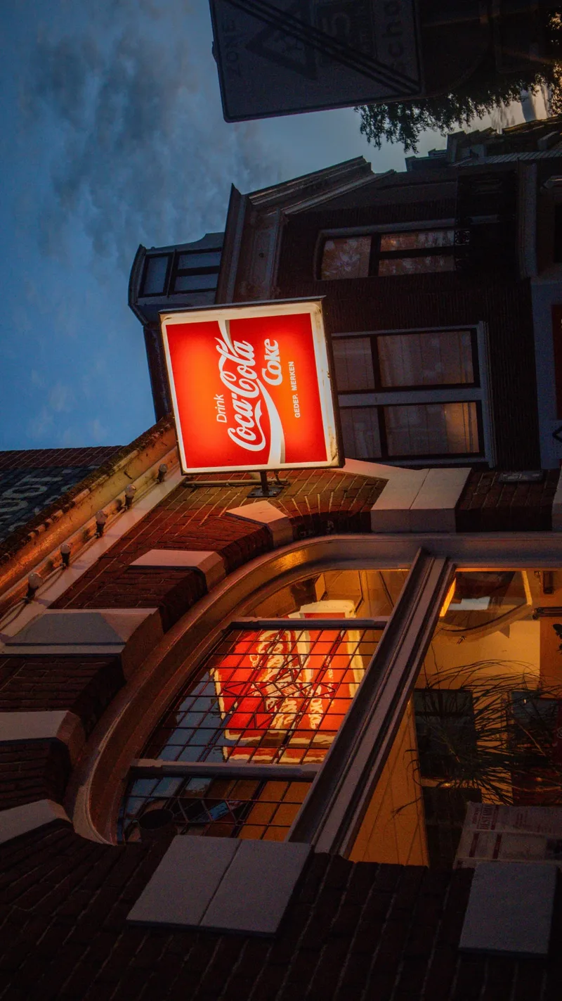 A red Coca-Cola sign on a corner building, seen from below