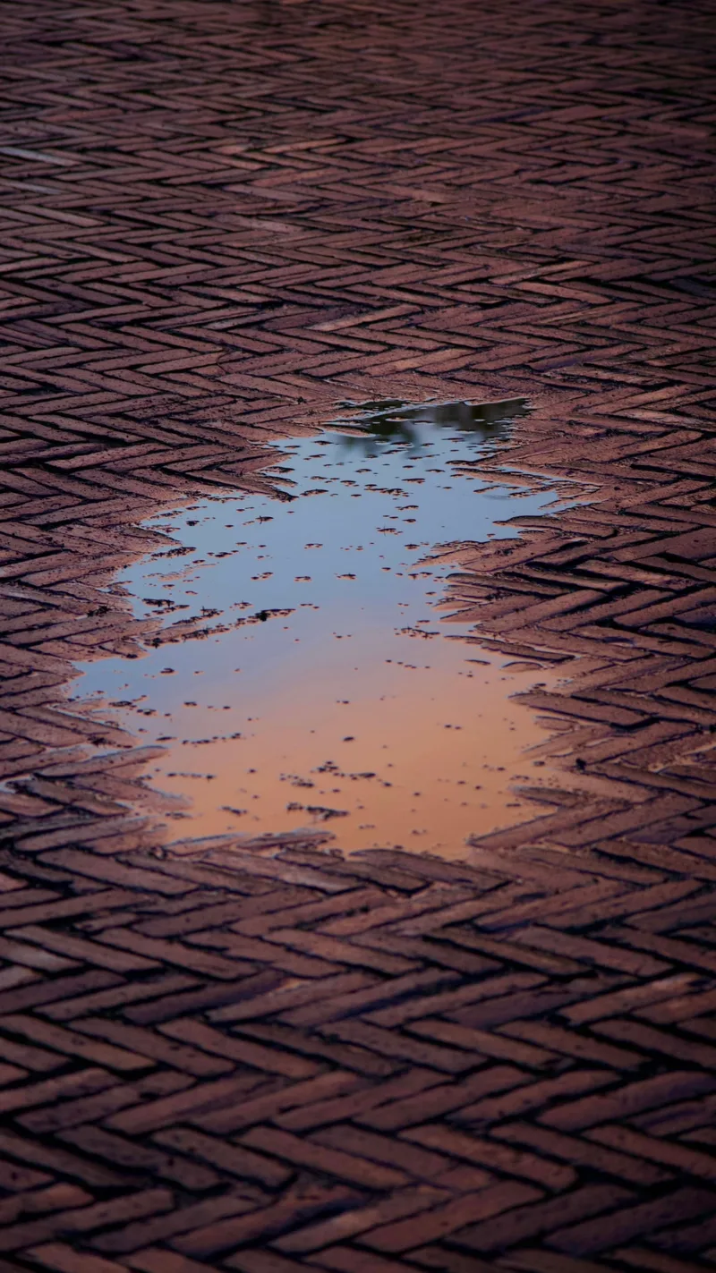 Sky reflected in a puddle on herringbone brick paving